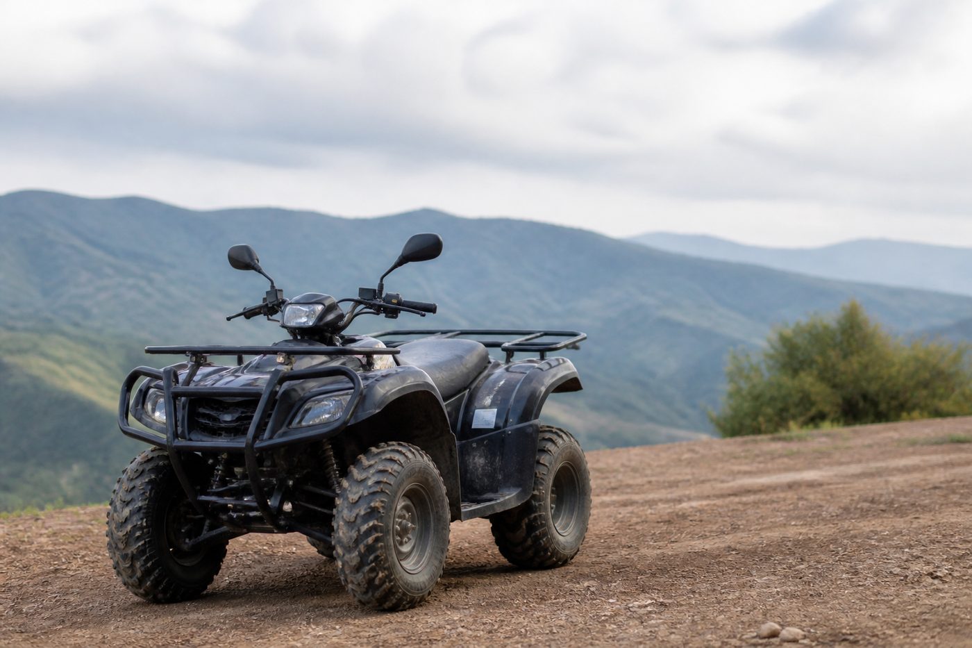 Toprak yolda duran bir ATV'nin ön sol tekerlek bölgesi yakın plan: çift A kollu bağımsız süspansiyon, yaylı amortisör ve dişli arazi lastiği